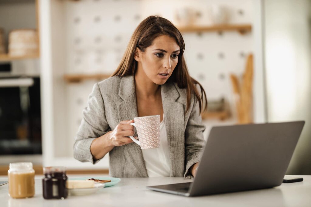 Frau, die vor ihrem Computer arbeitet und dabei einen Kaffee trinkt