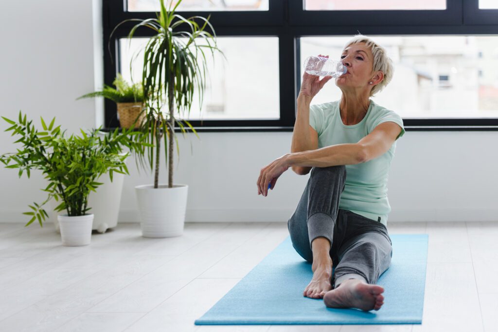 Eine ältere Frau trinkt Wasser nach einem Workout. -Ernährung