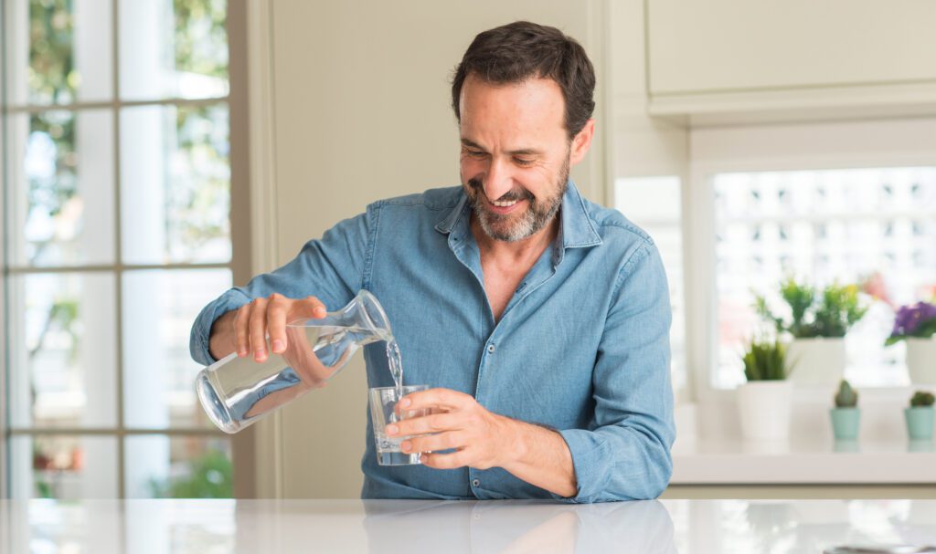 Ein Mann schenkt sich Wasser ein zur Grippe Prävention.