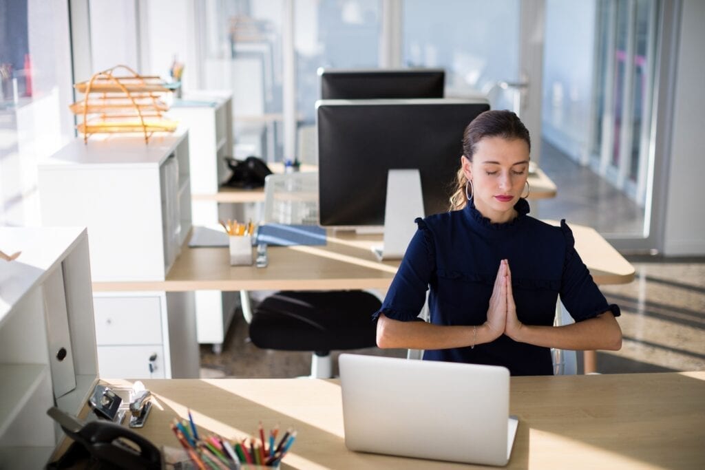 Eine Frau am Arbeitsplatz meditiert gegen ihre Rückenschmerzen