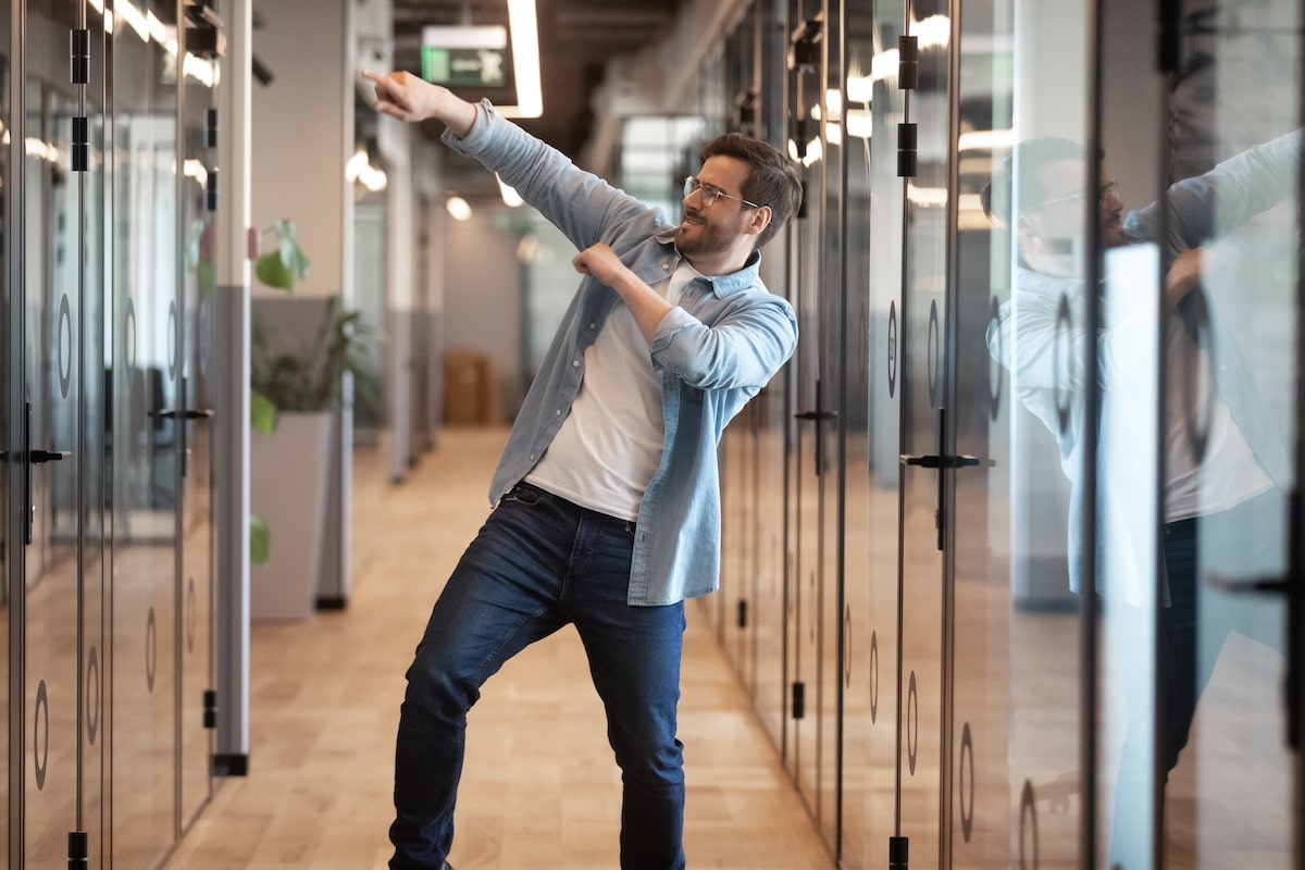 Overjoyed funny male coworker having fun performing winner dance in modern office hallway, excited happy millennial businessman celebrating business success or promotion, Friday night, end of work week